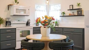 Eine moderne Küche mit einem runden Esstisch, dunklen Schränken, einer weißen Mikrowelle und einer Vase mit Blumen.