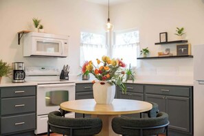 A modern kitchen with a round dining table, dark cabinets, a white microwave, and a vase with flowers. - Boutique 1BR Retreat, chilled & heated cowboy pool (Driftwood)