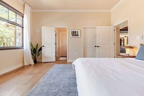 A bedroom with a large bed, a grey rug, a potted plant, and a door with a sign. - Boutique Hill Country Estate with viewing turret (Driftwood)