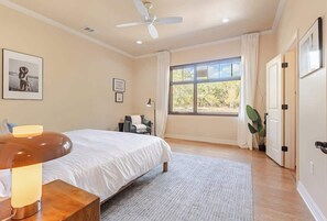 A bedroom with a bed, a bedside table with a lamp, a ceiling fan, a window with curtains, and a door. - Boutique Hill Country Estate with viewing turret (Driftwood)