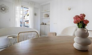Ein modernes Wohnzimmer mit einem Holzesstisch, weißen Sofas und einem Blumenstrauß.