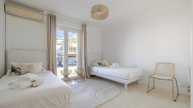 Une chambre d’hôtel avec deux lits, un coin salon avec un fauteuil, un balcon avec vue et un lustre moderne.