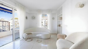 Un salon moderne avec un canapé aux lignes courbes, deux petites tables d’appoint et une grande fenêtre agrémentée de rideaux.