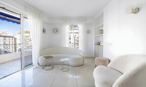 Ein modernes Wohnzimmer mit einer gebogenen Couch, zwei kleinen Beistelltischen und einem großen Fenster mit Vorhängen.