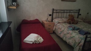 Una habitación pequeña y sencilla con una cama individual, una mesita de noche, una silla y un osito de peluche.
