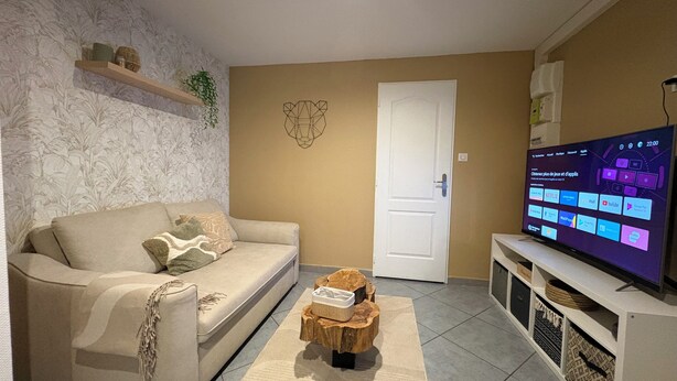 Een woonkamer met een beige bank, een salontafel, een televisie en een deur.