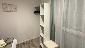 Een kamer met een bed, een witte inloopkast, een klein bankje en een wandplank.