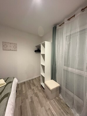 A room with a bed, a white wardrobe, a small bench, and a wall-mounted shelf. - Ground-floor apartment with a terrace and private parking. (Saint-Dié-des-Vosges)