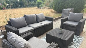 Een set rieten tuinmeubels met kussens, een bijzettafeltje en een tapijt met een patroon.