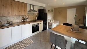 Een moderne keuken met houten kastjes, een inbouwoven en een eethoek met een houten tafel en stoelen.