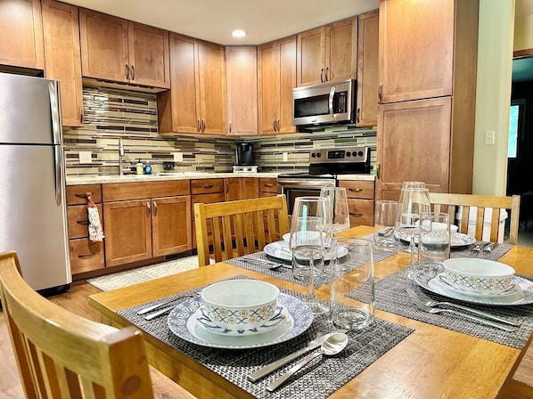 A modern kitchen with wooden cabinets, stainless steel appliances, and a dining table set for four.