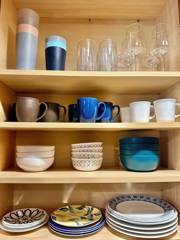 A wooden shelf with various kitchenware items including mugs, glasses, bowls, and plates.