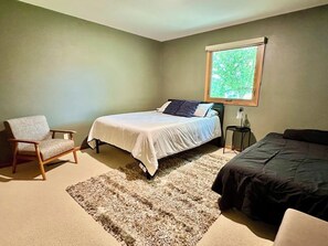 A bedroom with a bed, a chair, a nightstand, and a window.