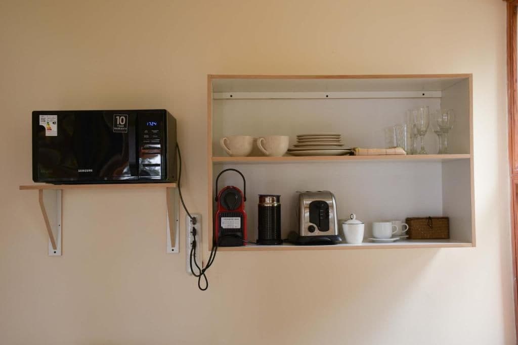 Uma cozinha equipada com micro-ondas, cafeteira e uma prateleira com chávenas e pratos.