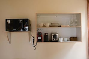 A kitchen with a microwave, a coffee maker, and a shelf with cups and plates.