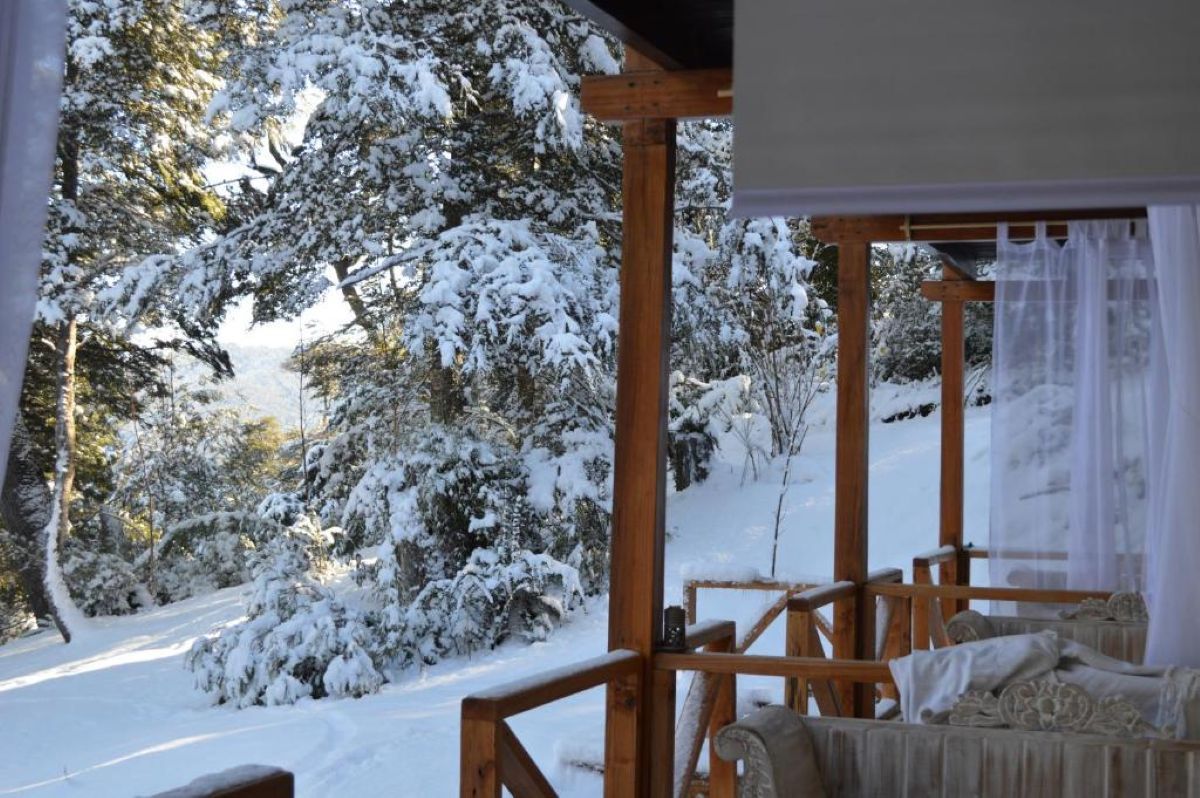 Um deck de madeira com uma cama e vista para árvores cobertas de neve.