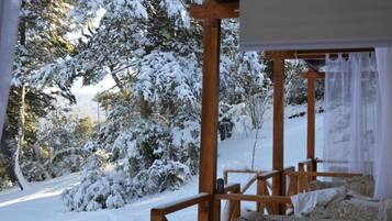 Um deck de madeira com uma cama e vista para árvores cobertas de neve.