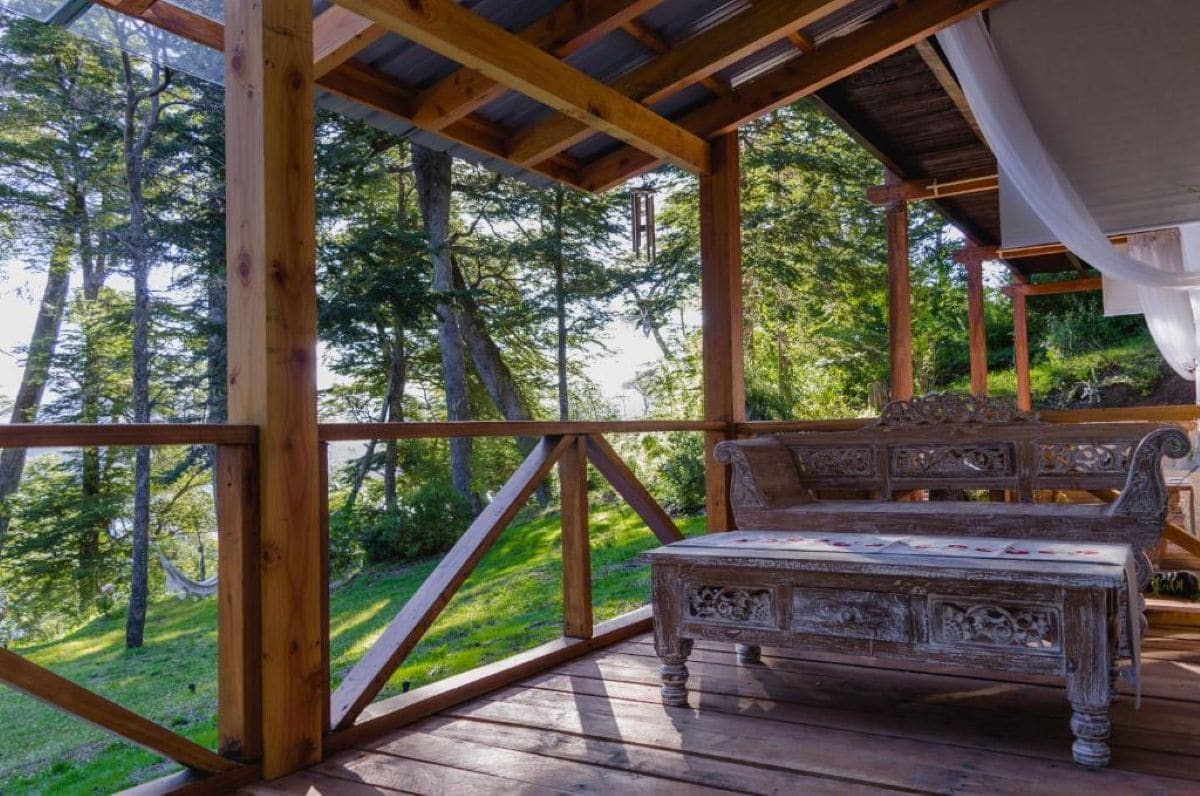Une terrasse en bois avec un banc, entourée d’arbres.