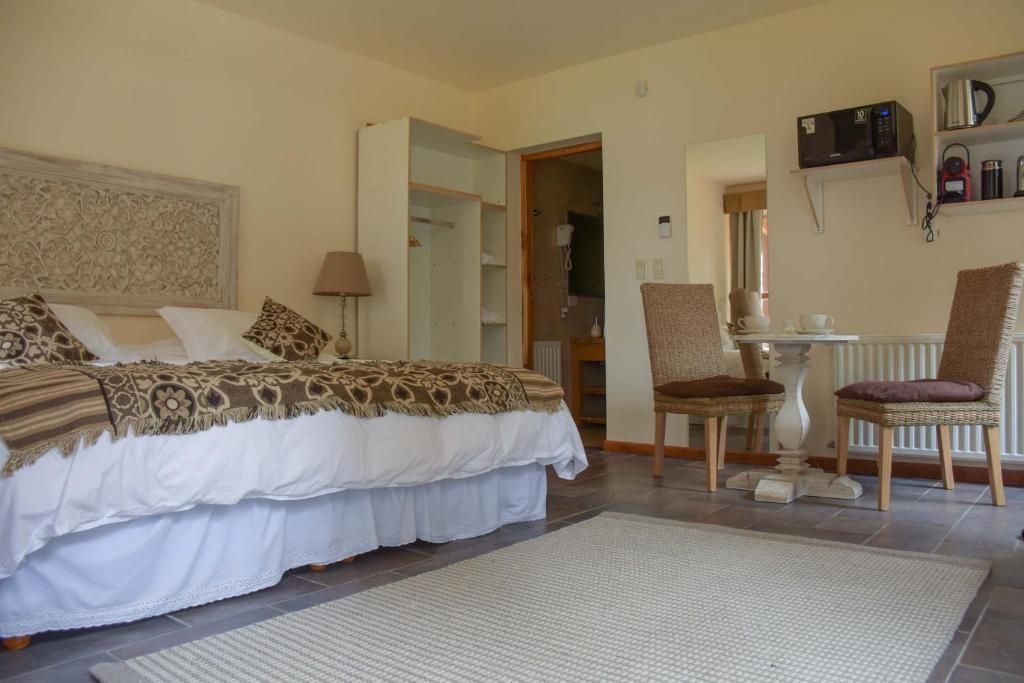 Quarto com cama, uma cadeira, uma mesa e prateleira com objetos.
