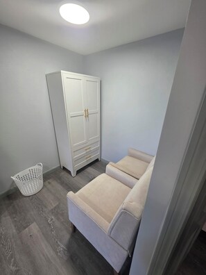 Ein Schlafzimmer mit einem weißen Kleiderschrank, einem beigen Sofa und einem weißen Wäschekorb.