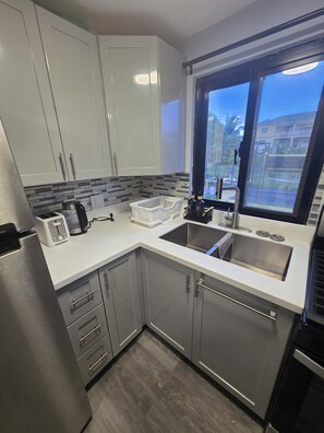 A modern kitchen with white cabinets, a stainless steel refrigerator, a toaster, and a window with a view of the outside. - Welcome to Modern Maison 

Tranquil studio apartment located in beautiful Nevis (Nevis)