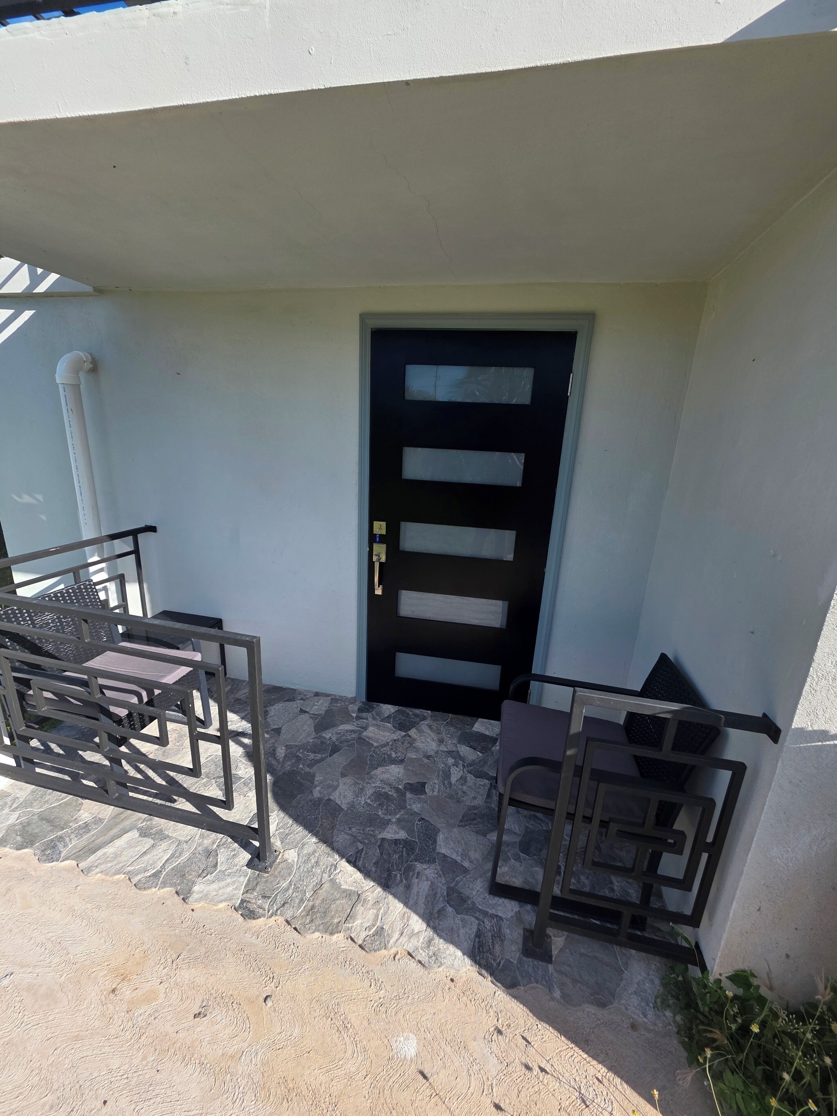 Entrada de un edificio con puerta negra, reja de metal y mesas al aire libre.