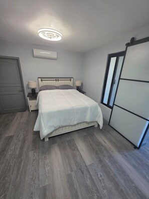 A bedroom with a bed, bedside tables, a ceiling light, a wardrobe, and a door. - Welcome to Modern Maison 

Tranquil studio apartment located in beautiful Nevis (Nevis)