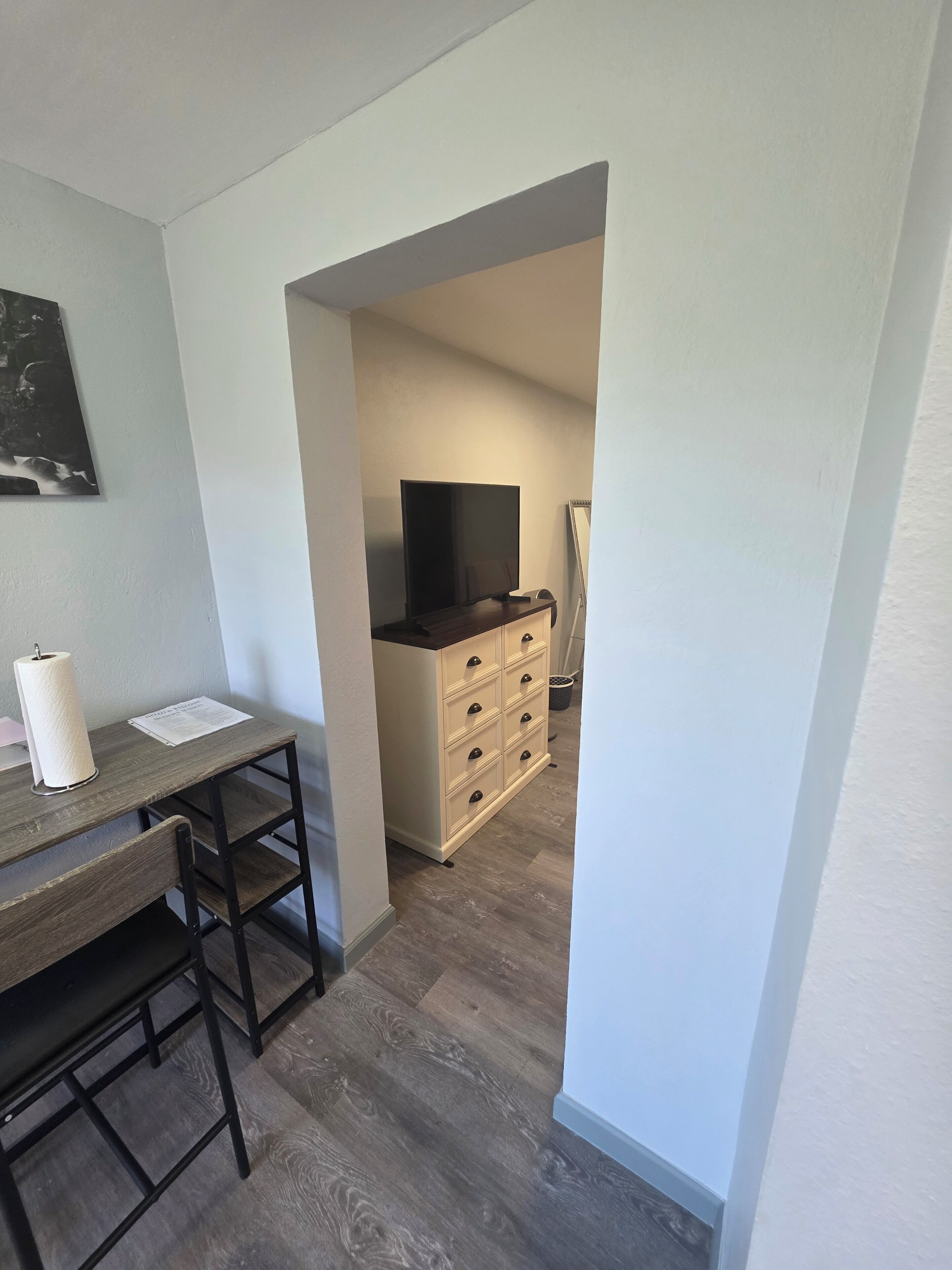 Una habitación con un escritorio de madera, televisor sobre un mueble bajo y cómoda con cajones.