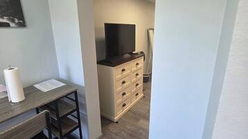 Una habitación con un escritorio de madera, televisor sobre un mueble bajo y cómoda con cajones.