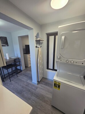 A compact kitchen with a built-in washer-dryer, a dining area with a table and chairs, and a window with curtains. - Welcome to Modern Maison 

Tranquil studio apartment located in beautiful Nevis (Nevis)