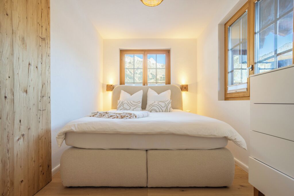Ein Schlafzimmer mit Bett, Nachttischlampen, einem Fenster mit Bergblick und einer Holzwand.