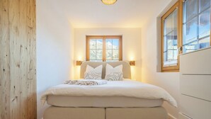 A bedroom with a bed, bedside lamps, a window with a mountain view, and a wooden wall. - Unique Chalet, Mountain View, Terrace, Gstaad (Château-d’Œx)