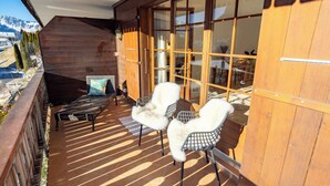 A wooden deck with a sofa and chairs, a glass door leading inside, and a view of the mountains. - Unique Chalet, Mountain View, Terrace, Gstaad (Château-d’Œx)