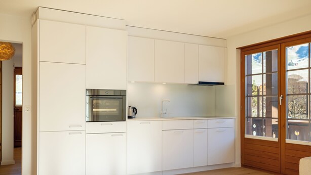 A modern kitchen with white cabinetry, a built-in oven, and a window with a view. - Unique Chalet, Mountain View, Terrace, Gstaad (Château-d’Œx)