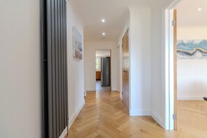 A hallway with wooden flooring, white walls, and a door leading to a room with a painting. - Family Friendly 4 Bedroom House in Rayleigh (Essex)