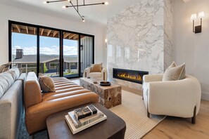 A modern living room with a fireplace, a sofa, a coffee table, and a view of the outdoors. - Gorgeous 3-bedroom 3-bath (Park City)
