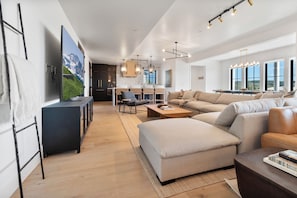 A modern living room with a large flat-screen TV, a sofa, a coffee table, and a dining area with a table and chairs. - Gorgeous 3-bedroom 3-bath (Park City)