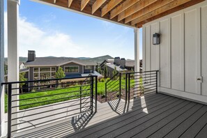 Ein überdachter Außenbereich mit Holzdeck, Metallgeländer und Blick auf Häuser und Hügel im Hintergrund.