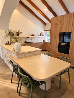 A modern kitchen with a stone island, wooden cabinets, and a built-in oven. - The Bale @ Quindalup. Secluded 4-bedroom bushland retreat on Quindalup Hill (Quindalup)