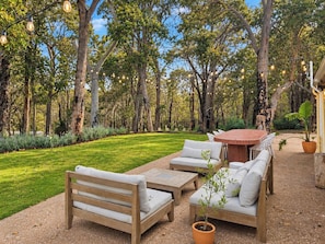 An outdoor seating area with wooden furniture, a round table, and string lights. - The Bale @ Quindalup. Secluded 4-bedroom bushland retreat on Quindalup Hill (Quindalup)