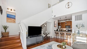 A modern living room with a flat-screen TV, a dining area with a glass table, and a kitchen with wooden cabinets. - Brooklyn Arts Condo | Walk to Live Oak & Dining (Wilmington)