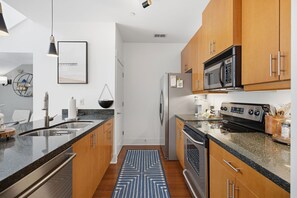 Een moderne keuken met roestvrijstalen apparatuur, houten kastjes, een granieten aanrecht en een hanglamp.