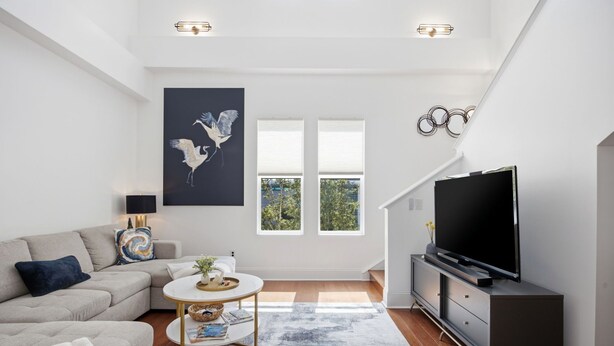 A modern living room with a sofa, a coffee table, a TV, and a large window with blinds. - Brooklyn Arts Condo | Walk to Live Oak & Dining (Wilmington)