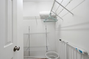 Um armário branco com prateleiras de metal, um radiador branco e uma cesto de roupa branca.