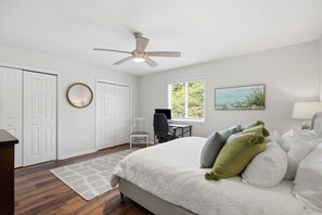 Une chambre à coucher comprenant un lit, un bureau, une chaise, un ventilateur de plafond et une fenêtre avec des stores.