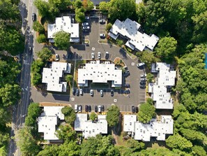 Vue aérienne d’un quartier résidentiel composé de plusieurs maisons individuelles, d’un parking et d’espaces verts environnants.