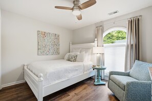 A bedroom with a bed, a chair, a ceiling fan, a window with curtains, and a wall-mounted artwork. - Minutes to Wrightsville Beach, Downtown & UNCW (Wilmington)