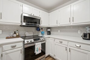 A modern kitchen with white cabinetry, a stainless steel stove, a microwave, and a coffee maker. - Minutes to Wrightsville Beach, Downtown & UNCW (Wilmington)