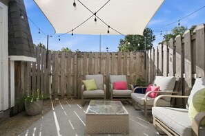 An outdoor patio area with a wooden fence, two cushioned chairs, a small table, and string lights. - Minutes to Wrightsville Beach, Downtown & UNCW (Wilmington)