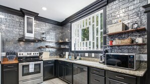A modern kitchen with dark cabinetry, a built-in oven, a microwave, and a window with a view of greenery. - The Jade Getaway in Historic Castle St. District (Wilmington)